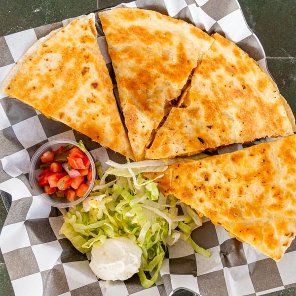 A golden-brown quesadilla cut into wedges, served with salsa, shredded lettuce, and sour cream.