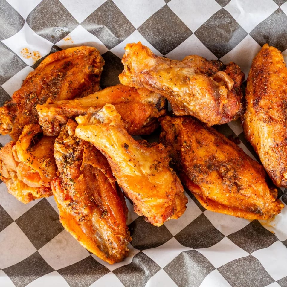A close-up of several crispy, seasoned chicken wings resting on black and white checkered paper.