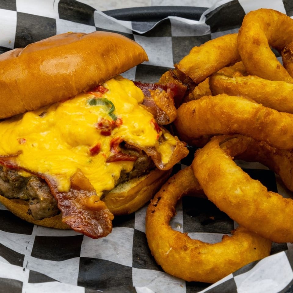 A cheesy burger with bacon and jalapeños, served with a side of golden onion rings.