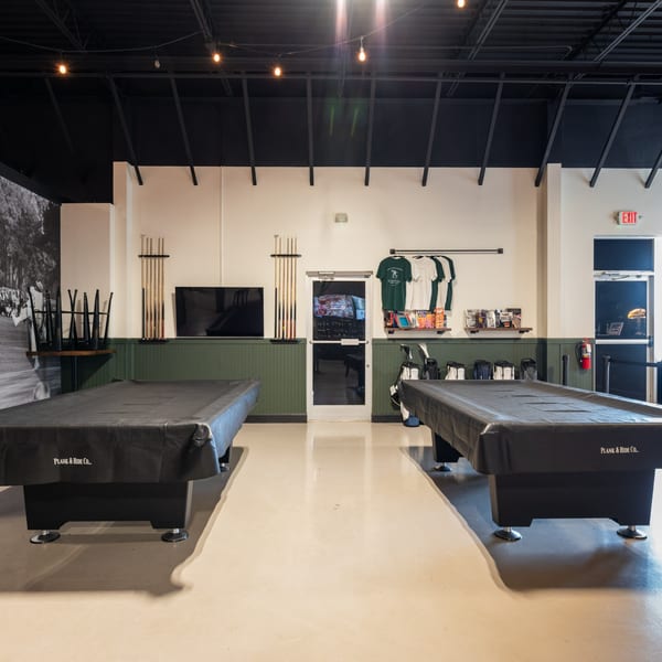 Two covered pool tables in a sports bar, with cue racks, TVs, and merchandise displays.