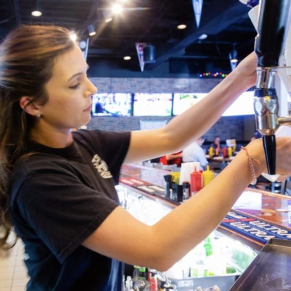 A bartender at 731 Sports Bar and Grill pours a beer from a tap, with TVs in the background.