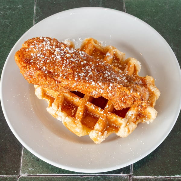Crispy fried chicken and a golden waffle, drizzled with syrup and powdered sugar on a white plate.