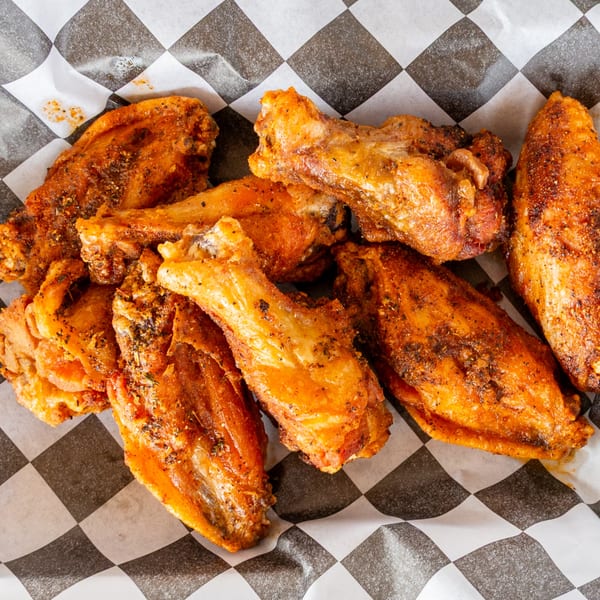 A close-up of several crispy, seasoned chicken wings on black and white checkered paper.